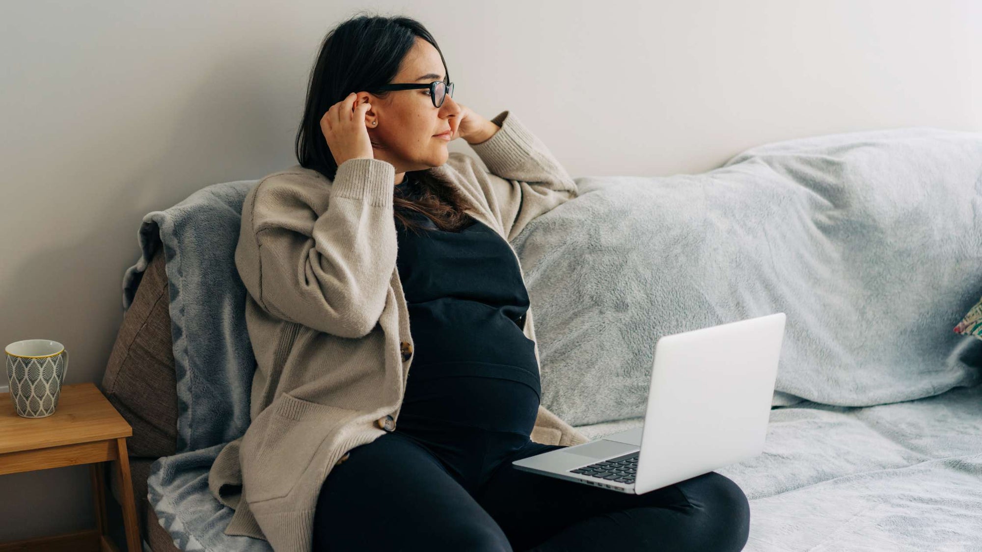 A pregnant woman sitting comfortably watching an online childbirth class at home on her laptop